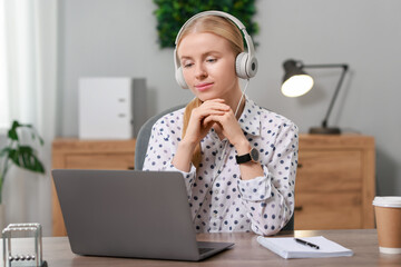 Interpreter in headphones working with laptop at table indoors