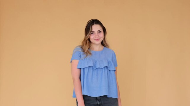Portrait of a happy and smiling Caucasian young adult woman, standing on beige background and looking at camera. People difference and individuality.