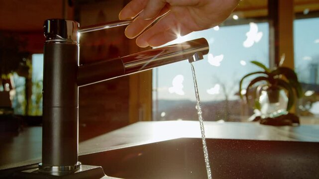 CLOSE UP, SLOW MOTION, LENS FLARE: Hand turns off tap above kitchen sink and water stops flowing. Golden light shines through window and casts a warm glow as clear waterdrops sparkle in evening light.