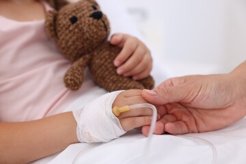 Mother and her little daughter with IV drip on bed in hospital, closeup