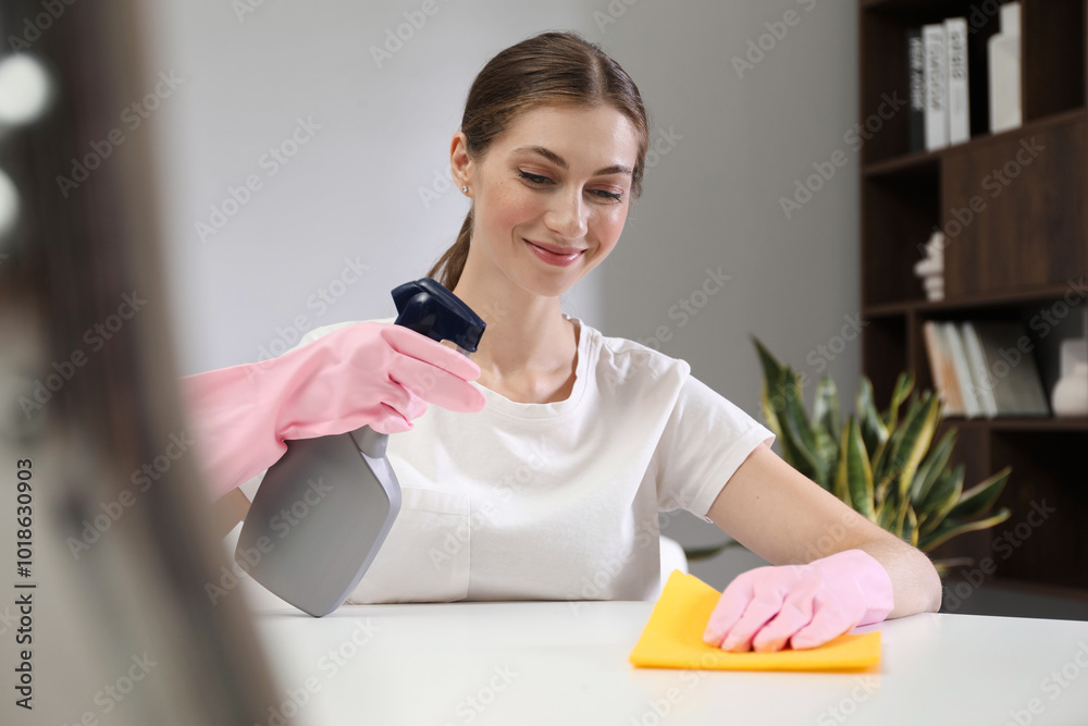 Sticker Young woman cleaning table with rag and spray in office