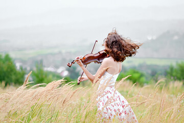 A girl plays the violin beautifully, against the backdrop of nature and mountains. © Мария Исак