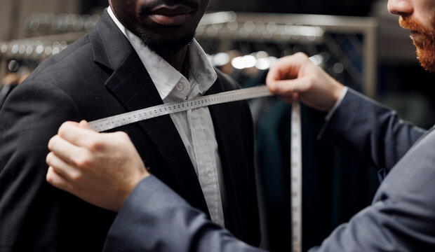 Professional tailor measuring client African American man for bespoke suit in luxury designer atelier
