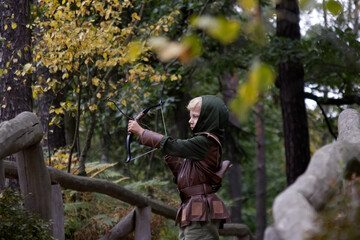 A boy in a medieval costume holding a bowstring against a forest background