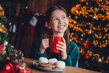 Photo of charming little girl drink cacao look empty space dressed green christmas garment tradition atmosphere decor house indoors room