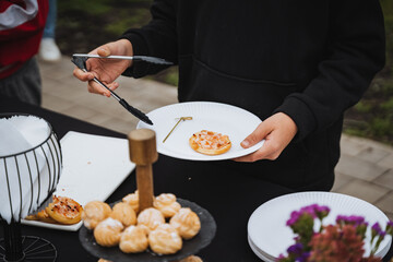 A person confidently holds a vibrant plate of colorful foods with tongs, ready to serve at a social event, showcasing culinary skills and inviting others to enjoy the meal