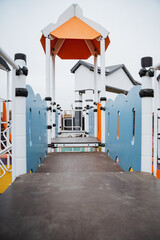 In the vibrant playground, a charming bridge elegantly leads toward a lovely house that is nestled in the inviting background, creating a picturesque scene for visitors to enjoy