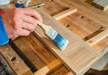 carpenter applies glue to surface of board with brush in carpentry workshop