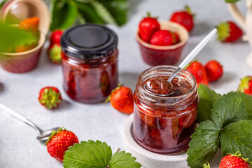 Jar of delicious homemade strawberry jam with a spoon scooping out the jam