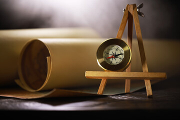 Compass on Wooden Stand with Rolled Paper Background in Soft Ambient Light