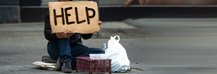 A beggar on a city street holding a cardboard with 