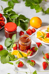 Jars of strawberry jam surrounded by fresh strawberries and orange slices
