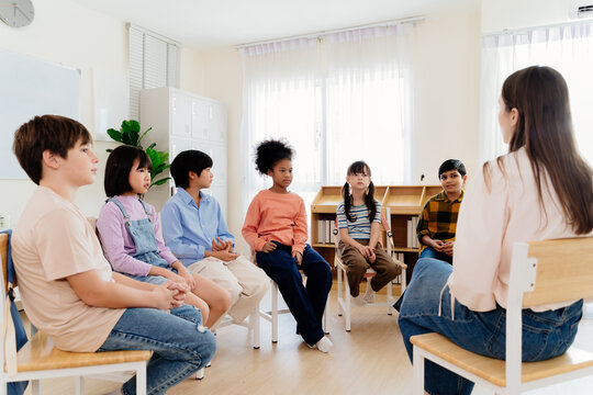 Group study session with diverse students seated in a circle engaging in a classroom discussion led by a teacher, emphasizing interactive learning and participation in a primary education environment