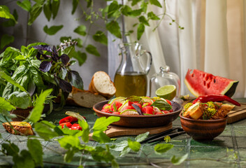 Fresh watermelon salad surrounded by herbs and spices on green tiled surface