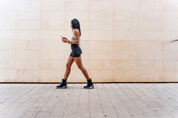 Trendy woman walking with determination in the street against the wall.