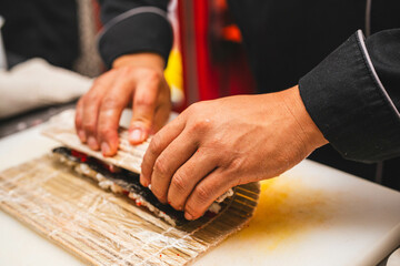 Close-up of a chef’s hands tightly rolling sushi using a bamboo mat. Perfect for sushi-making...