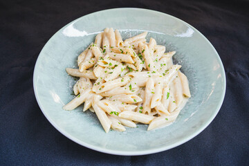 Side view of creamy penne pasta in a cheese sauce, garnished with herbs, served on a plain plate....