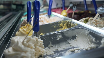 Close-up of a gelato display at an ice cream shop, showcasing various flavors with metal scoops ready for serving. A tempting and colorful scene capturing the allure of sweet treats