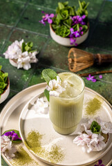 Glass of iced matcha latte decorated with flowers and matcha powder