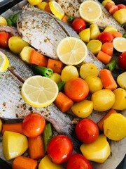 Fish on a baking tray decorated with potatoes, tomatoes and green peppers