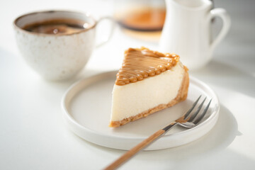 Salted caramel cheesecake and cup of coffee on white table. Coffee break
