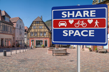 Shared space sign with a blurred small town marketsquare in background to illustrate the urban design approach that minimises the segregation between modes of road users.
