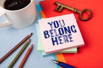 You belong here. Notepad with text, coffee mug and golden key on office table