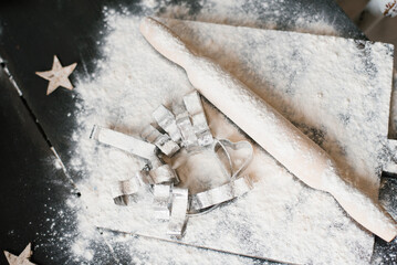 Wooden rolling pin sits on a table covered in flour. A heart-shaped cookie cutter next to the...