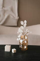 Glass vase with white flowers sits on a table next to two candles. Simple and elegant, with a sense of calmness and serenity