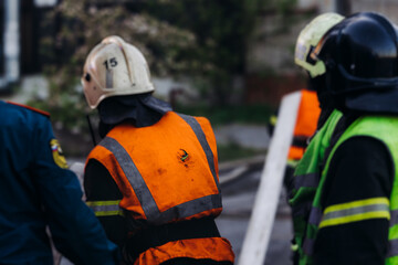 Obraz premium Group of fire men in uniform during fire fighting operation in the city streets, firefighters with the fire engine truck vehicle in the background, emergency and rescue, fire drill, exercise training