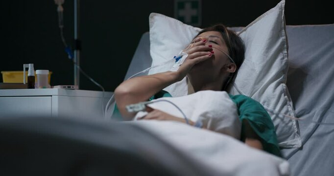 Young ill female patient in hospital ward with tube in nose lying in bed.