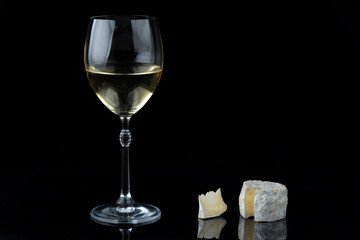 Traditional French goat cheese Crottin de Chavignol with a glass of white wine on a black background.