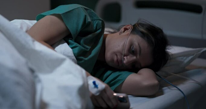 Young woman lying in bed, holding a phone, unable to sleep.