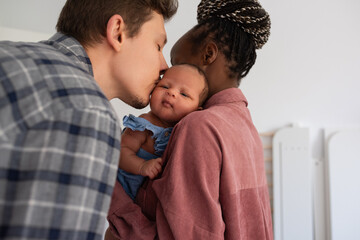 Father kissing baby carried by mother at home