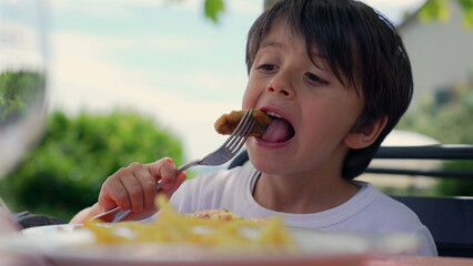 Young boy reacting to hot food, holding a fork with a piece of food and expressing surprise or discomfort, seated outdoors on a sunny day