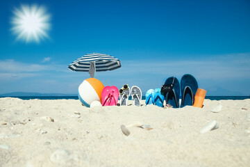 Obraz premium A Beach summer holiday banner background. Flip-flops and hat with a board and ball on the sand near the ocean. Summer accessories on the seashore. 