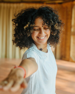 Smiling Woman with Curly Hair Reaching Forward in Indoor setting