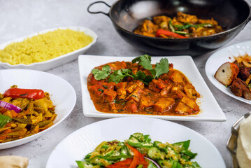 A central plate of curry with colorful vegetables and herbs, surrounded by an array of sides such as sautéed bell peppers, fresh salad with red onions, fluffy rice, and crispy bread.
