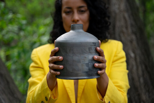 Holding Up Black Ceramic Jar In Nature