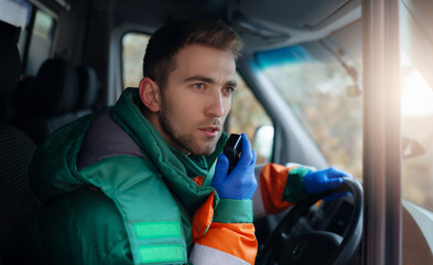 A male paramedic in a green and orange uniform is in an ambulance, using a radio to communicate...