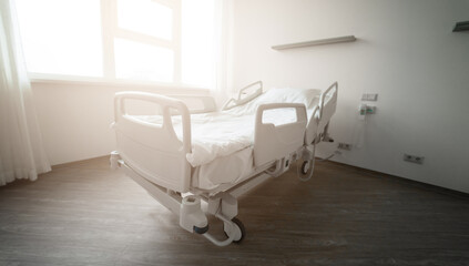 An empty hospital bed in a clean, modern room with soft sunlight coming through the window. The scene conveys a peaceful and sterile environment, ready for patient care and recovery.