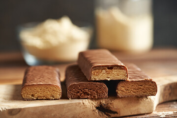 Four healthy protein chocolate bars with a bowl and jar of whey protein powder in the background