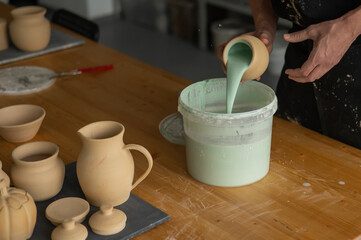 Close-up of a potter's hands glazing a pottery piece. 