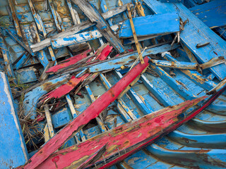 The bottom of an old, broken, wooden boat with peeling blue and red paint
