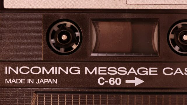 A tape recorder is playing an audio cassette. Close-up. A vintage audio cassette spins on a incoming message label tape used to record sound in a retro cassette player. Recording incoming calls.