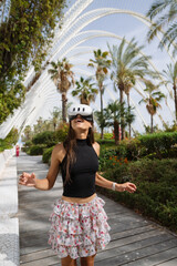 Fototapeta premium A young woman skating joyfully in a stylish summer outfit among palm trees on a sunny day