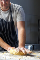 A chef in an apron kneads dough by hand, capturing the essence of the baking process. The focus is on the skillful technique of mixing ingredients, highlighting the traditional art of bread-making.