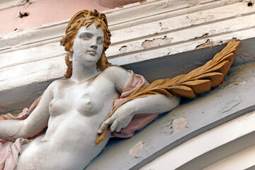 A weathered architectural sculpture of a female figure on a historic building facade in Sibiu, Romania. The figure is sculpted in a neoclassical style. 