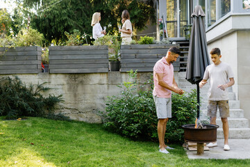 Female friends on terrace near father and son preparing grill