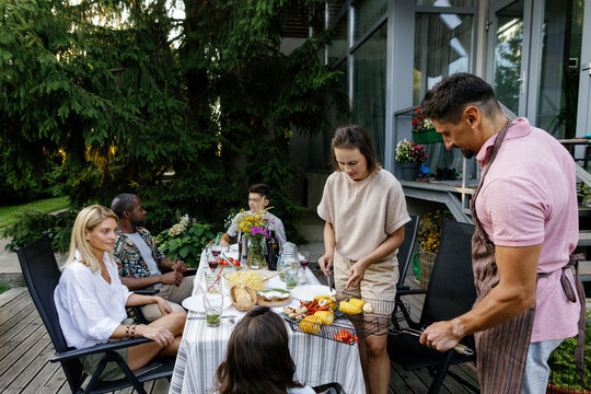 Man putting grilled vegetables on table with children and friends